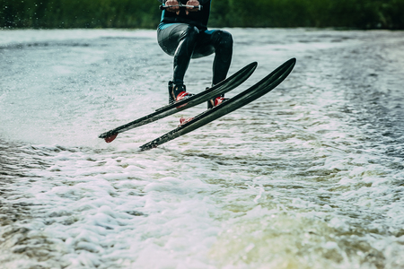 young man riding awater skis on lake in summer. jumping waves. body parts without a faceの写真素材