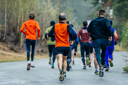 group of athletes men running down road in woods during marathon