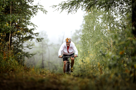 Revda, Russia - July 31, 2016: elderly male athlete mountainbiker rides in forest during Regional competitions on cross-country bikeのeditorial素材