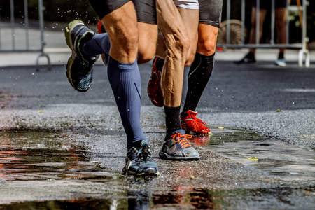 legs of three male marathon runners water splashes from under running shoesの写真素材