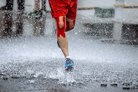 male athlete with tape on his knees running through a puddle of water, splashes and drops around feetの写真素材