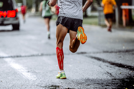 feet male athlete taping on calf muscles, running city marathon