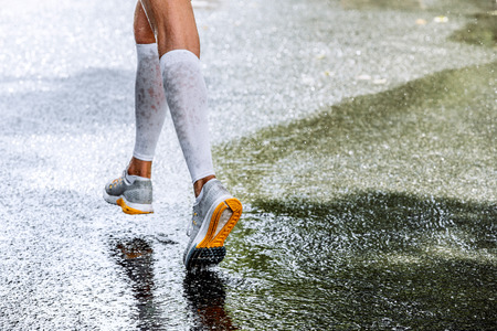 slender legs of women marathoner in compression socks, running through a puddle, water spraysの写真素材