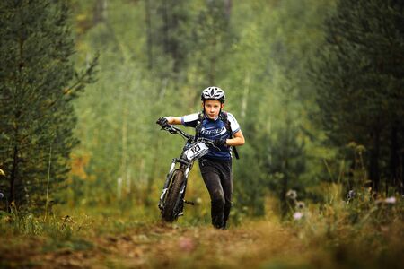 Revda, Russia - July 31, 2016: teen boy athlete mountainbike uphill on foot with his bicycle during Regional competitions on cross-country bikeのeditorial素材