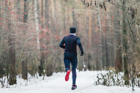 rear view athlete runner is running on a snowy trail in forest winter marathonの写真素材