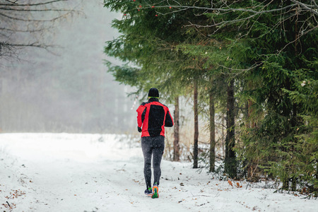 young male runner running in falling snow forest in marathon winterの写真素材