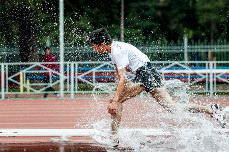 athlete runner in spray of water running steeplechase on track stadiumの写真素材