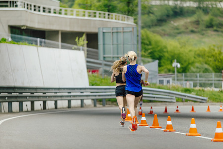 back two young women running in road with traffic cones safetyの写真素材