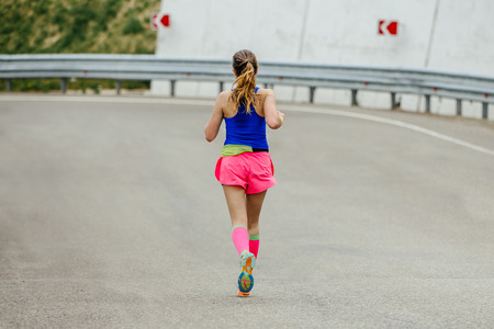 young woman runner in bright pink compression socks running on mountain roadの写真素材
