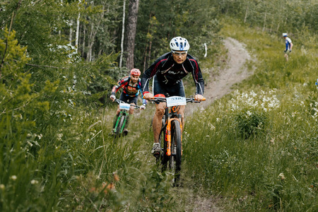 Revda, Russia - July 1, 2017: rivalry between two cyclists athletes on a forest trail during Regional competitions on mountain bikeのeditorial素材