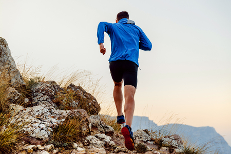 back runner man athlete running uphill trail over stonesの写真素材