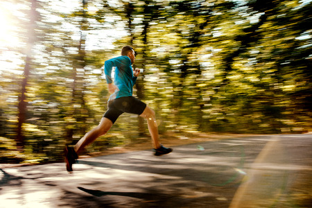 blurred motion male runner running on forest road in sunlight