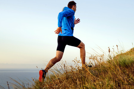 dynamic running uphill male athlete runner in background of sea and skyの写真素材