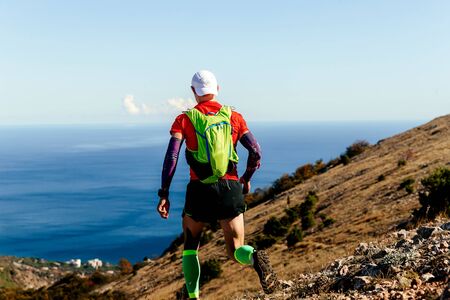 back athlete running mountain trail in compression socks on background of sea