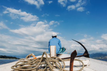 fisherman sit on nose of fishing boat with anchor and ropeの写真素材