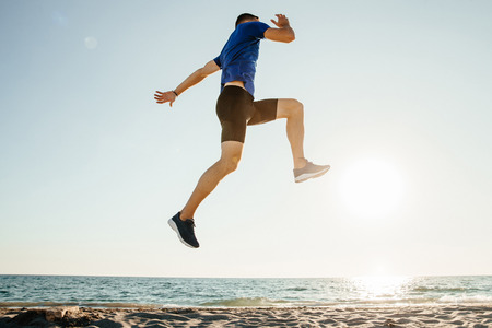 male athlete jump up and flying in sunlight on beachの写真素材