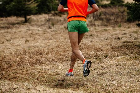 back male runner in bright orange shirt and green shorts running trailの写真素材