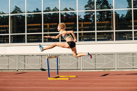woman athlete runnner running hurdles in summer athletics competitionの写真素材