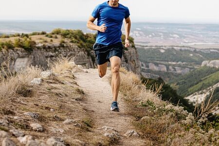 male runner running mountain trail on edge of cliff