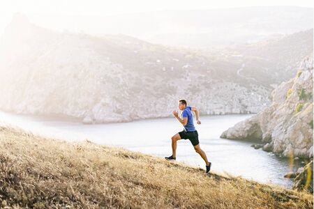 man athlete running uphill on background sea bay in sunsetの写真素材