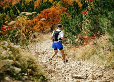 man with backpack and trekking poles down mountain on stone trailの写真素材