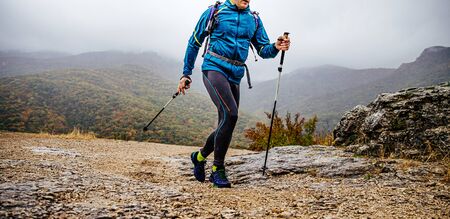 man with trekking poles walk mountain trail in rainy autumn weather