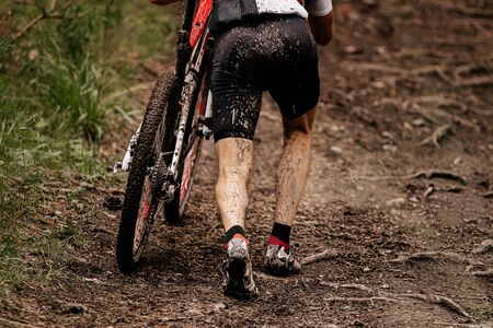 dirty legs cyclist walking uphill trail with mountain bikeの写真素材