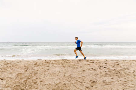male jogger run sandy beach in background of sea and skyの写真素材