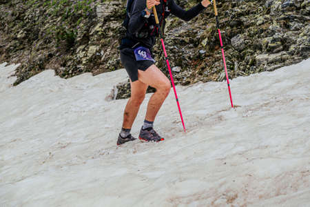 female athlete climbing uphill in snow with trekking poles
