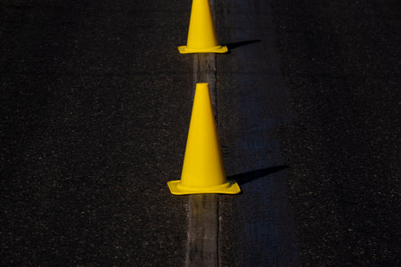 bright yellow safety cones on dark asphaltの写真素材