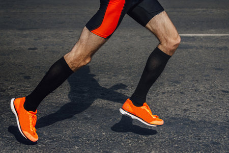 legs male runner in black compression socks and bright running shoes, shadow man jogger in dark...
