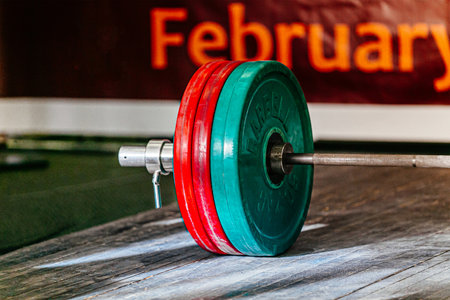 close-up barbell with red and green plates on wooden platform at powerlifting competition