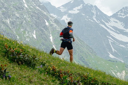 male athlete runner running down mountain marathon race on green meadow, background snowy peaksの写真素材