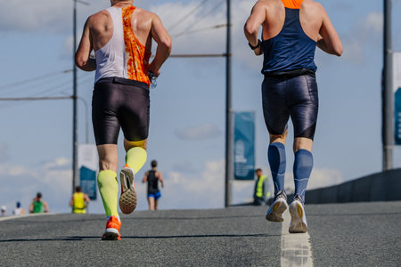 rear view two male athlete in compression socks running marathon race on road, summer sports eventの写真素材