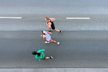 three athlete runners running on asphalt road, top-down view