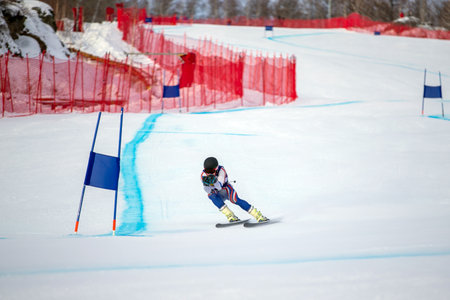 alpine skier racing downhill on snowy ski slope during giant slalom competitionの写真素材