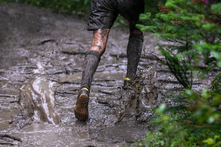Legs athlete running puddles of mud in heavy rain during forest marathon