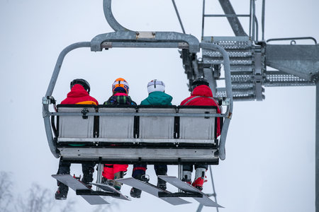 Four snowboarders on chairlift climb mountainの写真素材