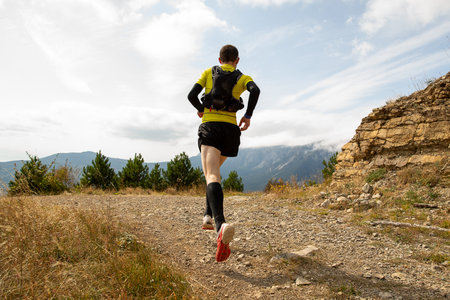 Male athlete in compression socks and hydration backpack running mountain marathon