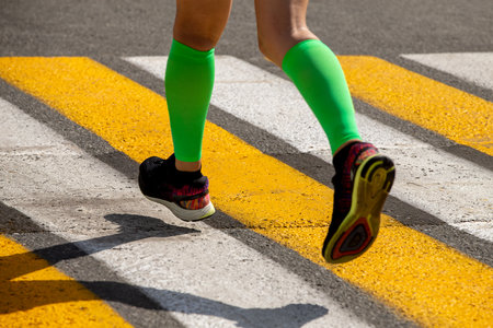 Woman runner legs in compression sleeves, running marathon on pedestrian crossingの写真素材