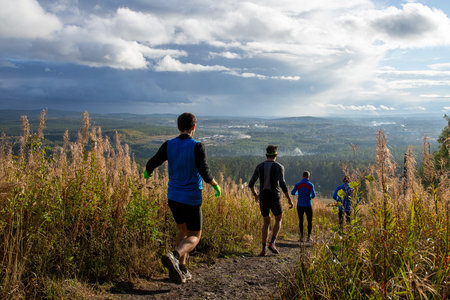 Four runners running one after other down trail from mountainの写真素材