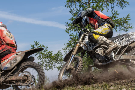 Ultra close-up shot two enduro riders battling through sharp muddy corner during race