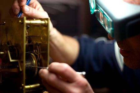 London Ontario, Canada - April 4, 2012.  Working at the same desk that his father did, Tom Buchenthal repairs the movement of a anniversary clock. Oxford Clock Shop was opened in 1954 by Tom's father Hans Buchenthal. The shop has been in the same locationのeditorial素材