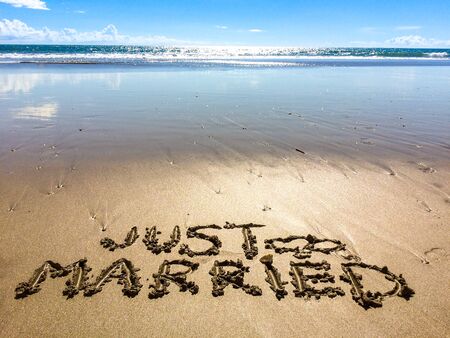 "Just married" written in sand during honeymoon in Bali, Indonesia. Blue sky and sea in the background.の写真素材