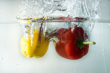 Vegetables in different colors, yellow and red, thrown into water to create splash effectの写真素材