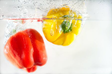 Vegetables in different colors, yellow and red, thrown into water to create splash effectの写真素材