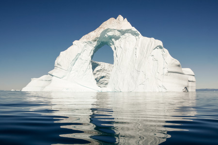 A lone iceberg floats in a still, deep blue sea.の写真素材