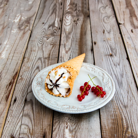 Ice cream with red currant in a waffle cone on wooden background.の写真素材