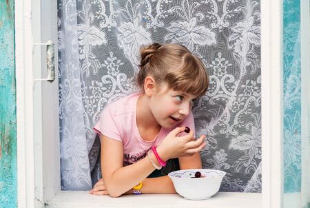 Little girl eats cherry in old russian cottage.の写真素材