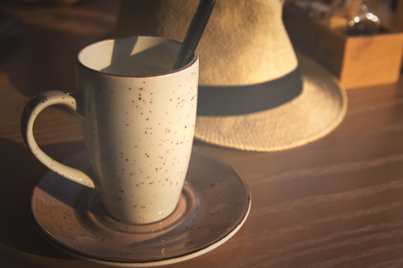 Evening latte cup in cafe with fedora hat on wooden table.の写真素材